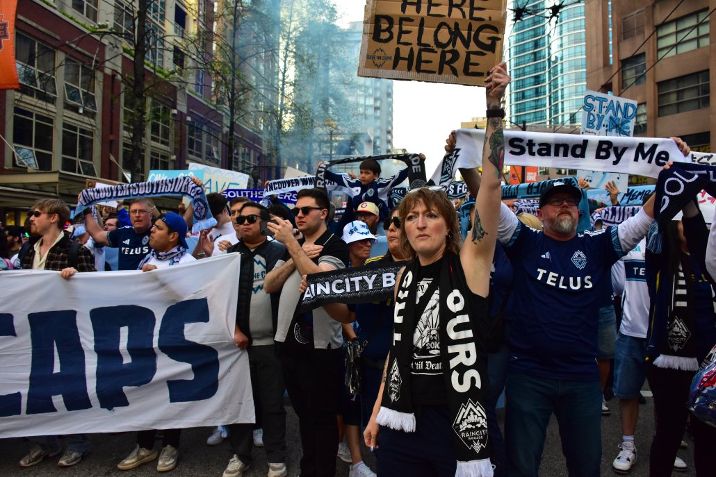 A large crowd of Vancouver Whitecaps supporters marches through downtown Vancouver streets holding signs and banners in support of keeping the team in the city.